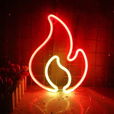 A neon sign shaped like a flame, lit up in red and yellow, is displayed against a tiled red background. There are some decorative flowers to the left and a reflective surface with star-like glitter below.
