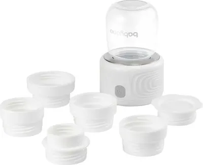 A white baby bottle warmer with several white bottle adapters arranged around it.