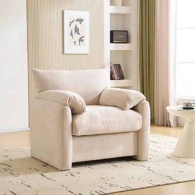 A beige armchair is placed in a living room setting, with shelves and curtains in the background.