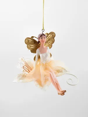 A decorative ornament of a fairy sitting on a flower, suspended by a gold string.