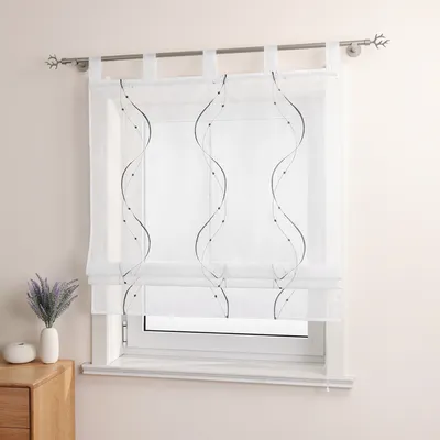 A white sheer curtain with embroidered wavy lines and dots hangs on a window.