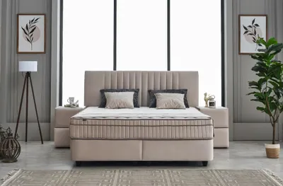 A bedroom scene featuring a beige boxspring bed with a headboard, two nightstands, a floor lamp, and artwork on the wall.
