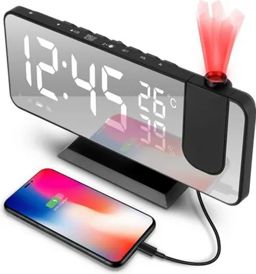 A digital alarm clock with a projected display and a smartphone charging on its base.