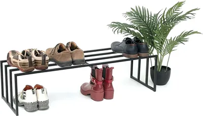 A black metal shoe rack with various shoes and boots placed on it, next to a potted green plant.