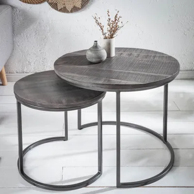 A set of two nesting coffee tables with round, grey wooden tops and black metal frames, placed on a white wooden floor.