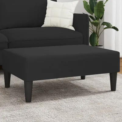 A black ottoman is placed on a light gray carpet in front of a black sofa.