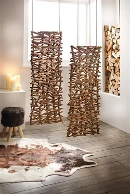 A room with wooden floors, featuring decorative rattan and wood room dividers, a cowhide rug, a stool, and candles.
