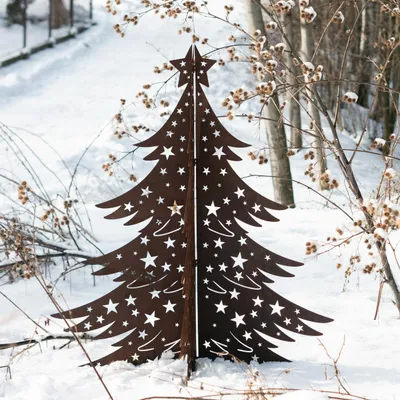 A metal Christmas tree decoration with star cutouts stands in the snow, surrounded by bare branches and dried seed pods.
