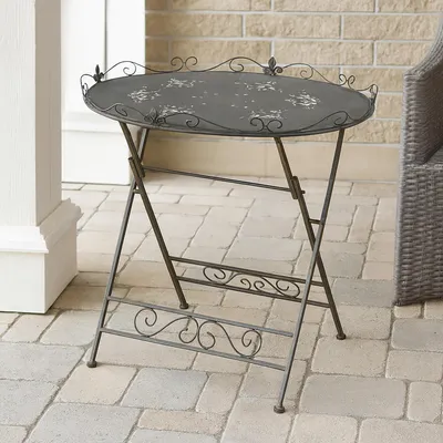 A small, round, folding table with a decorative edge and floral pattern on the tabletop, placed on an outdoor patio.