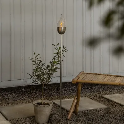 An outdoor setting with a solar-powered LED torch, a potted plant, and a bamboo bench.