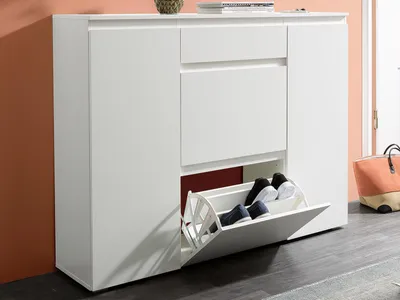 A white shoe cabinet with a pull-out drawer containing shoes, placed against an orange wall.