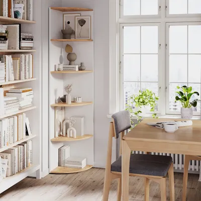 A corner shelf unit filled with books and decorative items, next to a window with plants and a dining table with a chair.