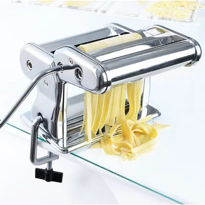 A pasta machine with fresh pasta coming out of it, on a glass table.