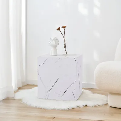 A cube-shaped side table with a marble-like pattern sits on a fluffy white rug in a well-lit room.