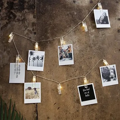 A string of LED lights with clips holding photos, displayed against a textured wall.