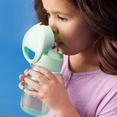 A young girl is drinking from a green straw bottle.