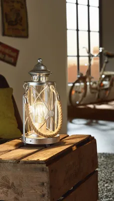 A vintage-style lantern lamp sits on a wooden crate next to a couch, with a bicycle visible in the background through a window.