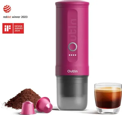 A pink portable espresso maker with coffee grounds and capsules next to it, and a shot of espresso in a glass.