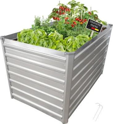 A raised garden bed filled with lettuce, herbs, and tomatoes, with a small sign indicating 'Deutsche Marke'.