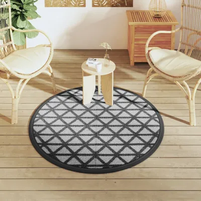 A round rug with a geometric pattern is placed on a wooden deck, with two wicker chairs and a small side table around it.