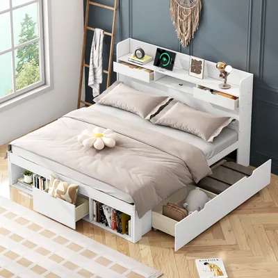 A bedroom scene featuring a white bed with storage drawers, a headboard with charging capabilities, and decorative items.