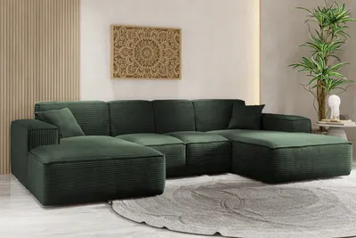 A large, dark green sectional sofa is arranged in a U-shape in a modern living room setting. The sofa has a textured fabric and appears to be modular. A circular gray rug is placed in front of the sofa, and a wooden wall art hangs on the wall behind it. A 
