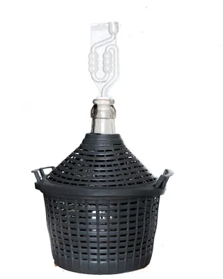 A glass carboy with a black plastic basket and a fermentation airlock.