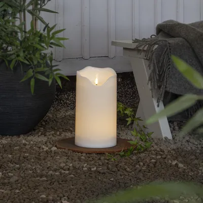 An LED candle is placed on gravel next to a potted plant and a bench with a blanket.