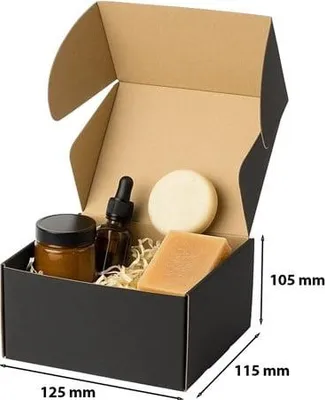 A black cardboard box with its flaps open, containing various cosmetic products and filler material. Dimensions are indicated on the side.