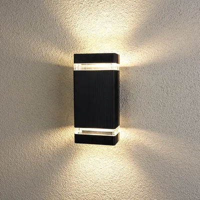 A black rectangular outdoor wall light mounted on a textured wall, emitting light upwards and downwards.