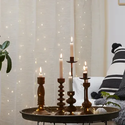 Candles on a tray in front of a curtain with fairy lights.