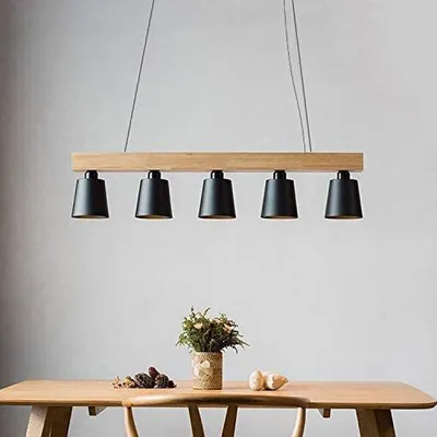 A modern pendant light fixture with a wooden beam and five black lampshades hangs above a wooden table.