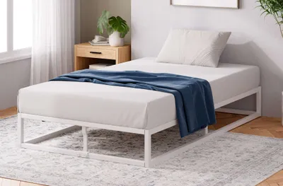 Modernes weißes Metallbett mit klaren Linien – gemütlich eingerichtet mit Teppich und Nachttisch.
