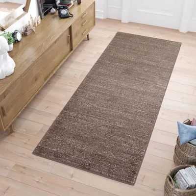 A long, narrow rug is laid out on a light wooden floor in front of a wooden cabinet.