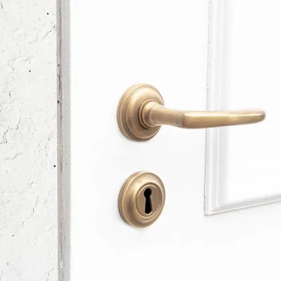 A close-up shot of a brass door handle and keyhole on a white door, with a textured white wall on the left.