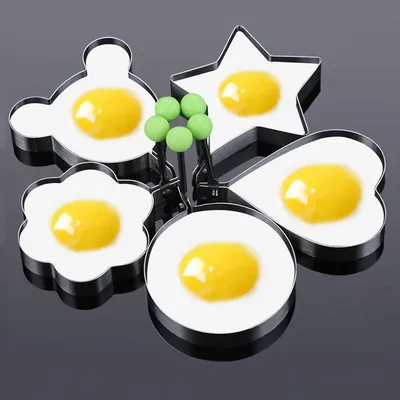 A set of five metal egg rings in various shapes, each containing a fried egg. The rings have green handles. The background is black.