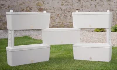 Five white planters stacked and arranged on grass in front of a stone wall.