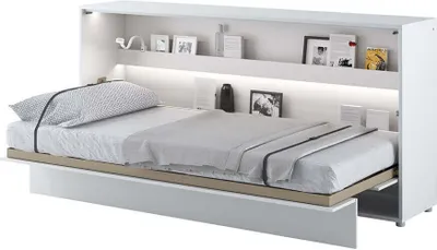 A white wall-mounted bed is shown in its open position, with the mattress and bedding laid out. Shelves are above the bed with decorative items.
