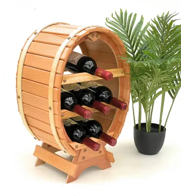 A wooden wine rack shaped like a barrel, holding six bottles of red wine, with a potted plant in the background.