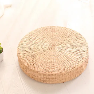 A round, woven floor cushion is placed on a light-colored wooden floor.