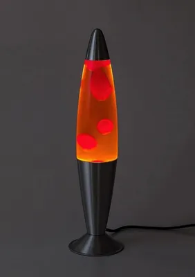 A lava lamp with red blobs in orange liquid sits on a dark gray surface.