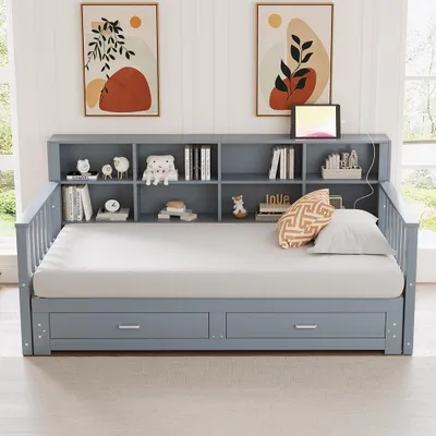 A gray wooden daybed with a built-in bookshelf headboard and two storage drawers underneath, set in a room with artwork on the wall and a window in the background.