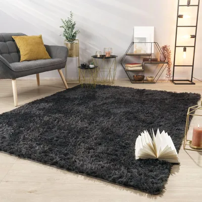 A living room scene featuring a dark gray shaggy rug, a gray armchair with a yellow cushion, and various decorative items on side tables and a shelf.