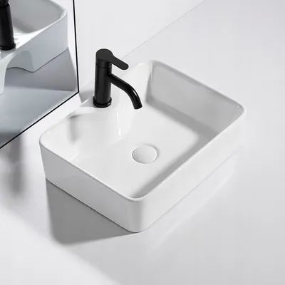 A white ceramic sink with a black faucet is shown on a white surface, with a mirror reflecting the sink and faucet.