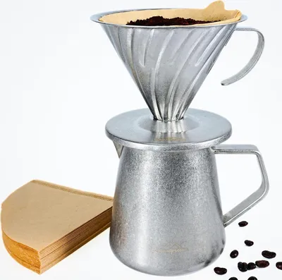 A stainless steel pour-over coffee maker with coffee grounds and a stack of paper filters.
