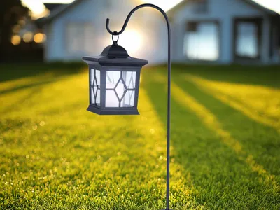 A solar lantern is mounted on a pole in a grassy yard with houses in the background during sunset.