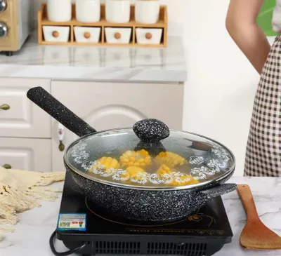 A person is cooking corn in a wok on an induction stove.