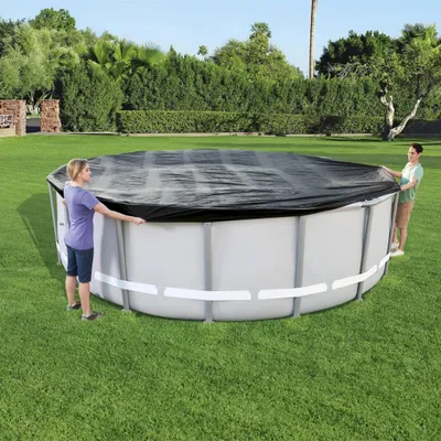 Two people are putting a cover on an above-ground swimming pool in a grassy backyard.
