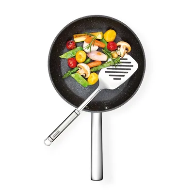 A frying pan with vegetables and a spatula.