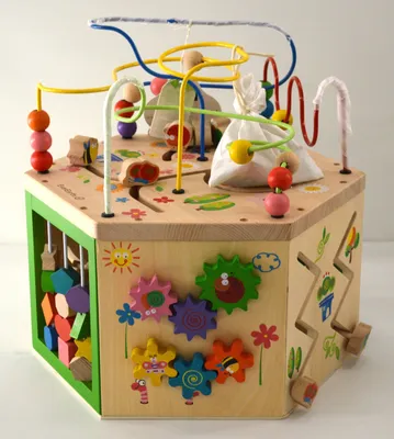 A hexagonal wooden activity cube toy with various interactive elements like beads, gears, and mazes, set against a plain white background.